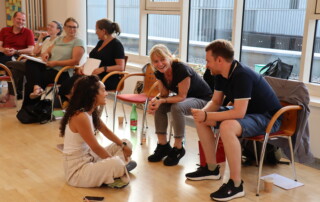 Teilnehmende sitzen im Seminarraum der il Akademie im Kreis und sprechen lachend miteinander.
